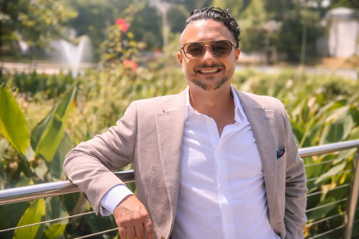 Johnny Tellez smiling in a light blazer by a garden railing